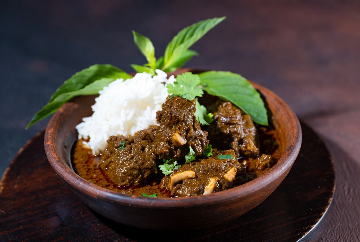 Dark Indonesian beef rendang with rice in a wooden bowl